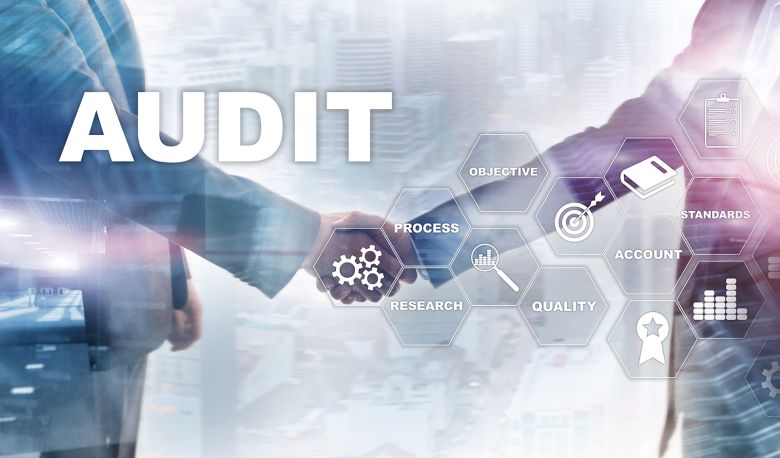 The word Audit is written large in the foreground, behind it stand two businessmen shaking hands