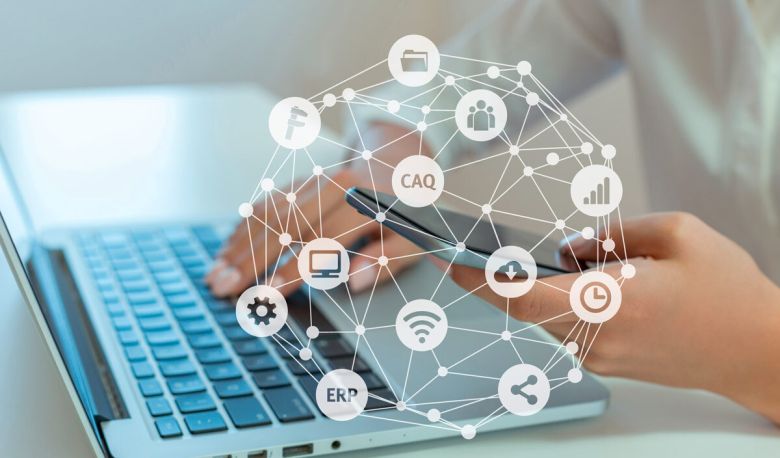 Net with various symbols such as CAQ, ERP, cogwheel, cloud and in the background sits a woman with a laptop and cell phone in her hand.