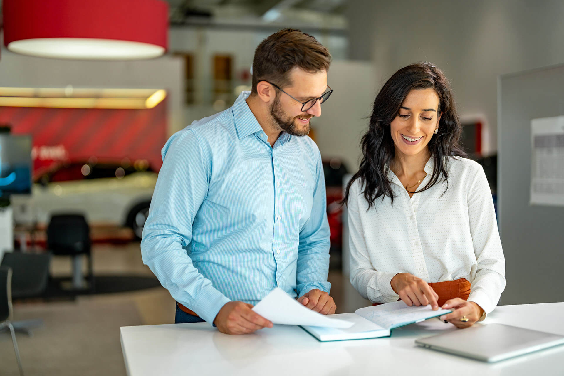 Two people stand in front of a desk and point to a book